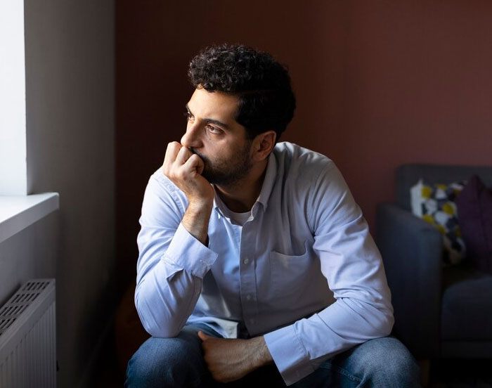 A man in a light shirt looks thoughtfully out the window, pondering a promotion decision.