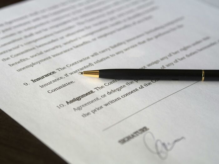 A black pen rests on a signed document, illustrating sneaky scams involving paperwork and contracts.