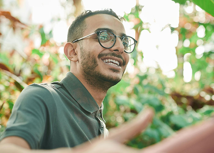 A smiling person with glasses and a beard in a green shirt, surrounded by lush greenery, symbolizing coming out reactions.