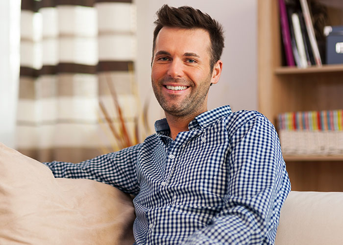 Smiling man in a checkered shirt, sitting on a couch, embodying memorable dad stories.