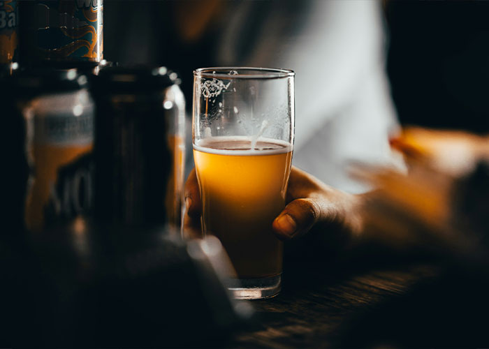 Hand holding a glass of beer, once considered exotic, on a wooden table next to cans.