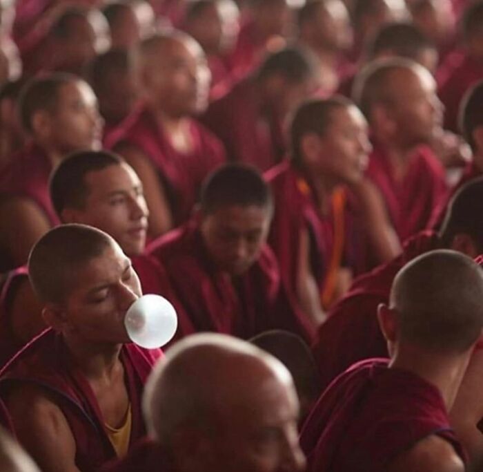 Monk blows bubble gum among others in robes, capturing a perfectly timed street photo.