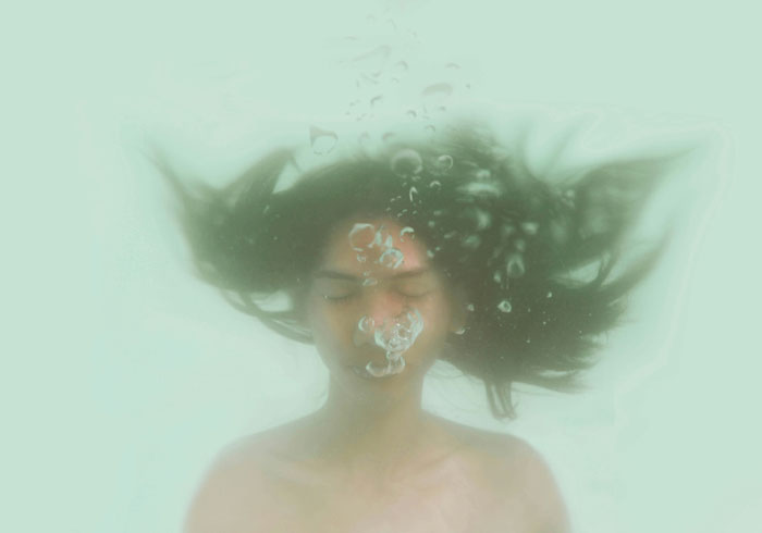 Person underwater, hair floating, exhaling bubbles; life-saving knowledge about breathing techniques could help in emergencies.