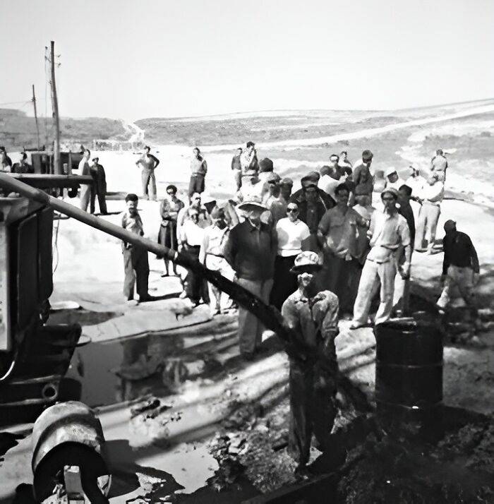 Historical turning point: a group gathers around an early oil rig in a barren landscape.