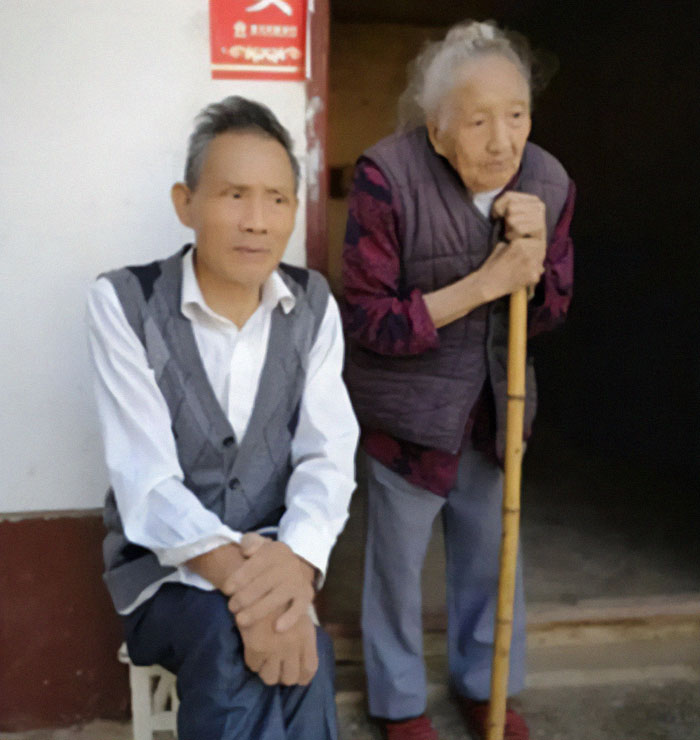 Elderly Chinese woman with a cane and man seated outside a home.
