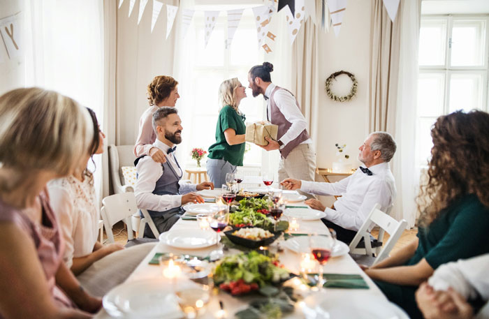 Man at rehearsal dinner table, embracing woman, surrounded by guests, with festive decor. Man at rehearsal dinner table, embracing woman, surrounded by guests, with festive decor.