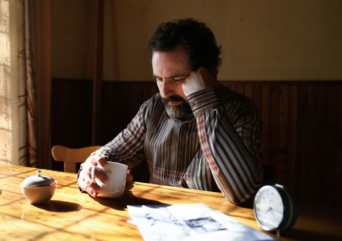 Man feeling empty, canceling wedding due to in-laws’ drunken behavior, sitting alone at a table with coffee. Man feeling empty, canceling wedding due to in-laws’ drunken behavior, sitting alone at a table with coffee.
