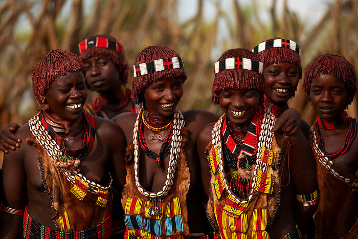 Smiling women in traditional attire with beadwork, showcasing global culture and tradition.