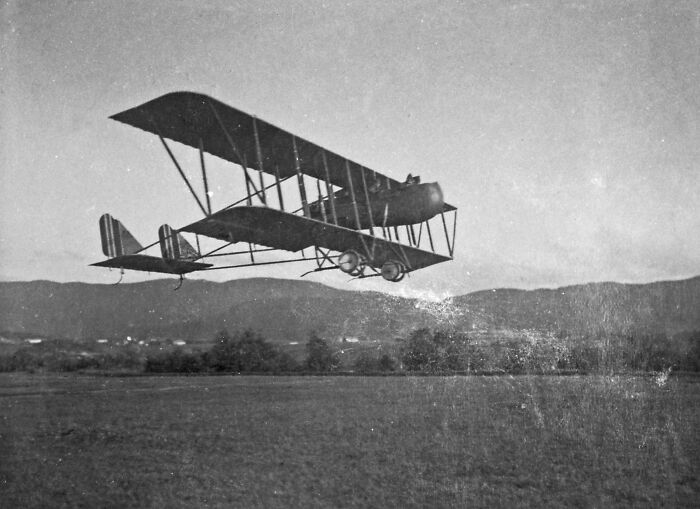 Vintage biplane in flight over open field, highlighting world changes over the past century.