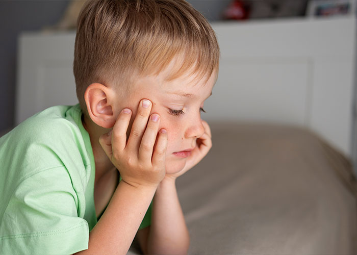 Sad child with a pensive expression, hands on face, illustrating effects of trashy parenting behaviors.