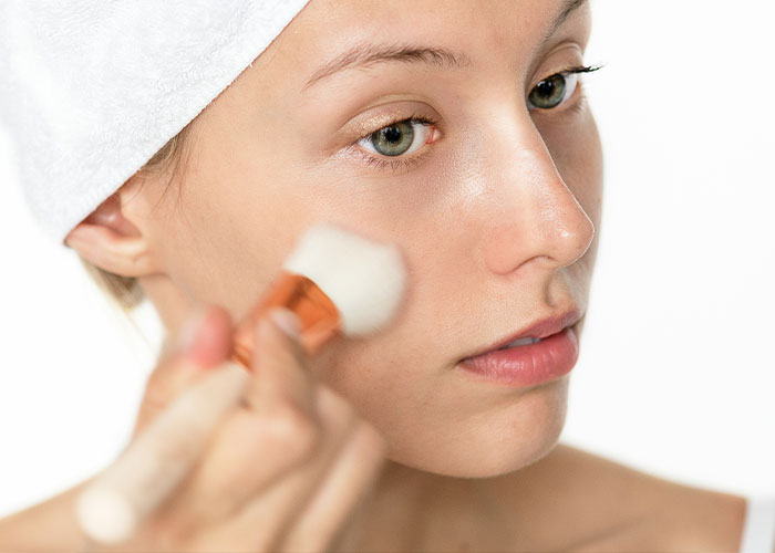 Woman applying makeup with brush, wearing a towel on her head, relating to unserious boycott reasons of brands.
