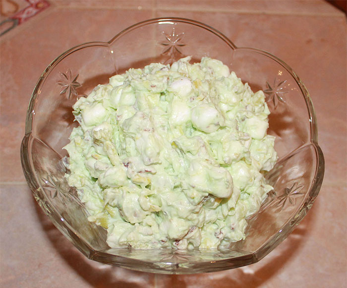 A bowl of creamy Watergate Salad with marshmallows and nuts in a decorative glass dish.