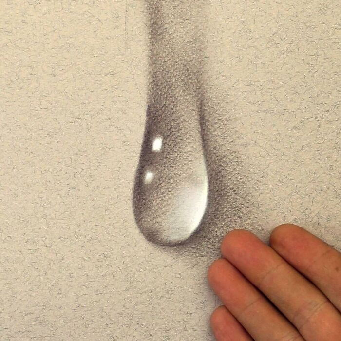 3D drawing by a German artist, depicting a realistic water droplet, with a hand nearby to show scale.