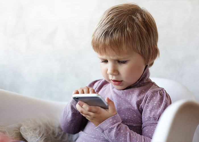 A young child focused on a smartphone, highlighting modern parenting concerns.
