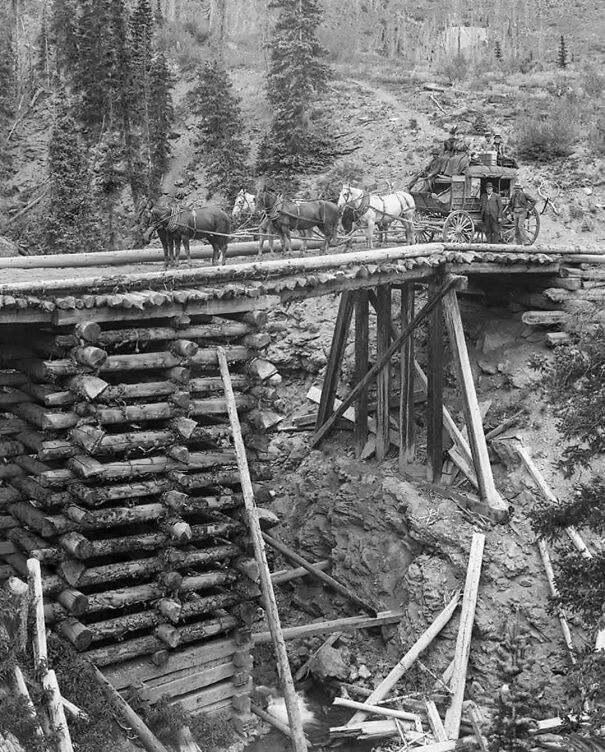 Horse-drawn carriage crossing a log bridge in a historical photo, offering a perspective of the past.