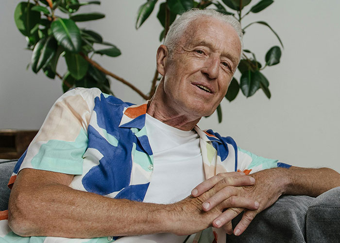 Elderly man in colorful shirt, sitting on a couch, smiling warmly; represents positive reactions to coming out.