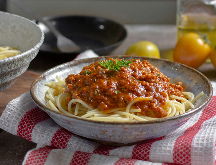 Bowl of spaghetti with meat sauce, garnished with parsley, showcasing a lazy meal idea in a cozy kitchen setting.