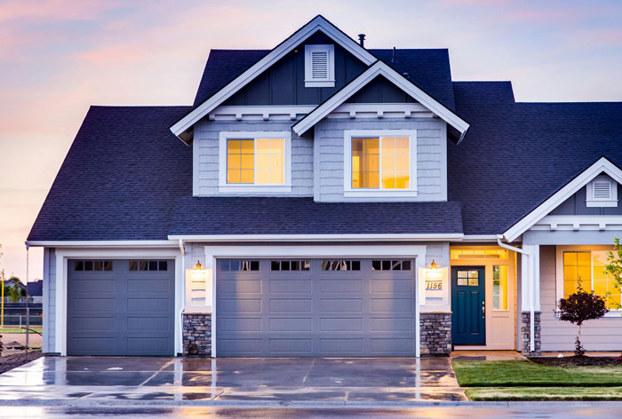 Modern American home exterior with three-car garage and lit windows at dusk.