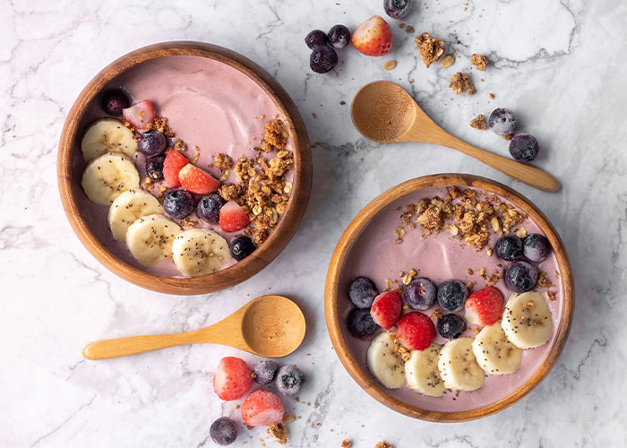 Smoothie bowls with banana, strawberries, blueberries, and granola, showcasing once exotic foods in a modern presentation.