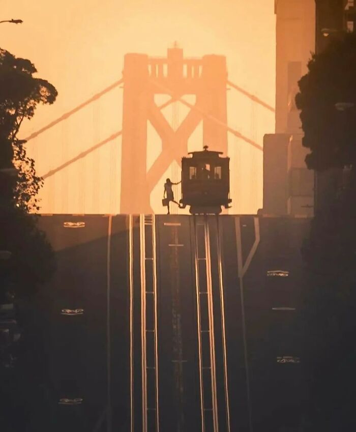 Perfectly timed street photo of a tram at sunset with a silhouetted person against the backdrop of a bridge.