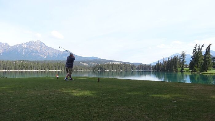 Golfer on a scenic course with mountains and lake, highlighting breathtaking golfing destinations worldwide.