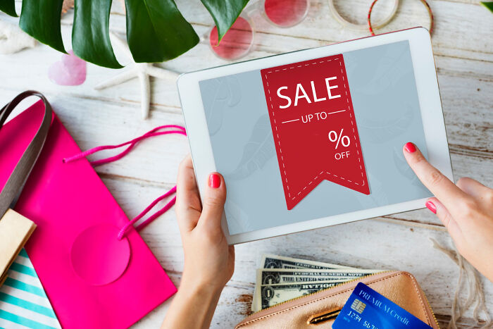 Tablet displaying a sale banner, surrounded by shopping bags and credit cards, illustrating old people habits.