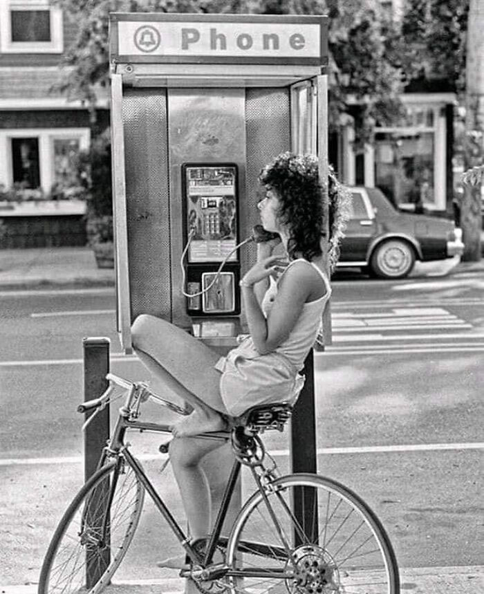 Person on a bicycle using a public phone in a nostalgic city setting, capturing forgotten history.