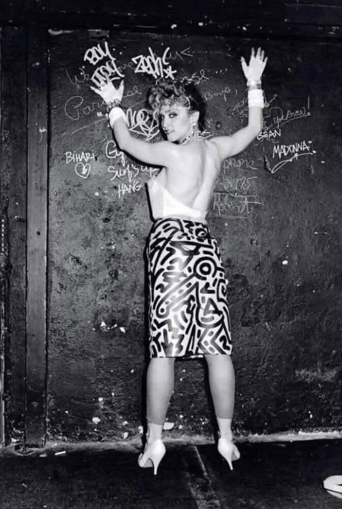 Individual in patterned skirt posing against a graffiti-covered wall, evoking forgotten corners of history.
