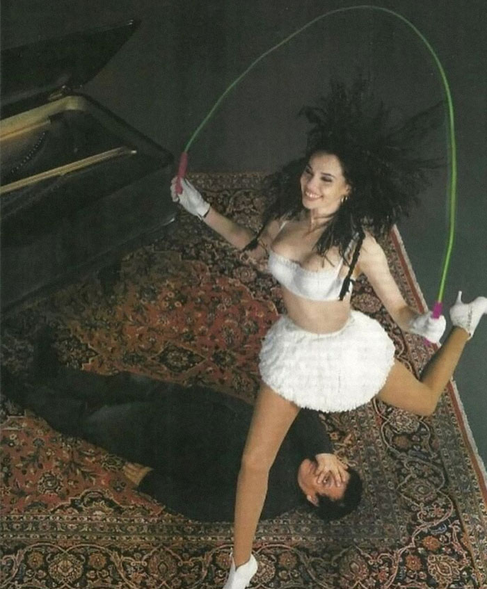 Woman skipping rope over a man on a carpet, embodying forgotten corners of history with a playful twist.