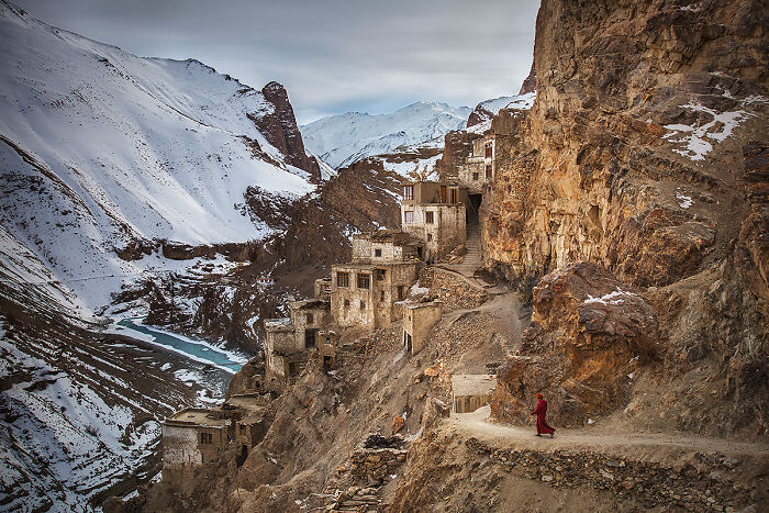 Monk walking on a mountain path near cliffside village, showcasing global culture and tradition in a remote setting.