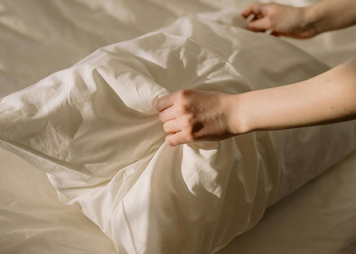 Hands adjusting a pillowcase on a bed, illustrating beauty tips for better sleep and skincare.