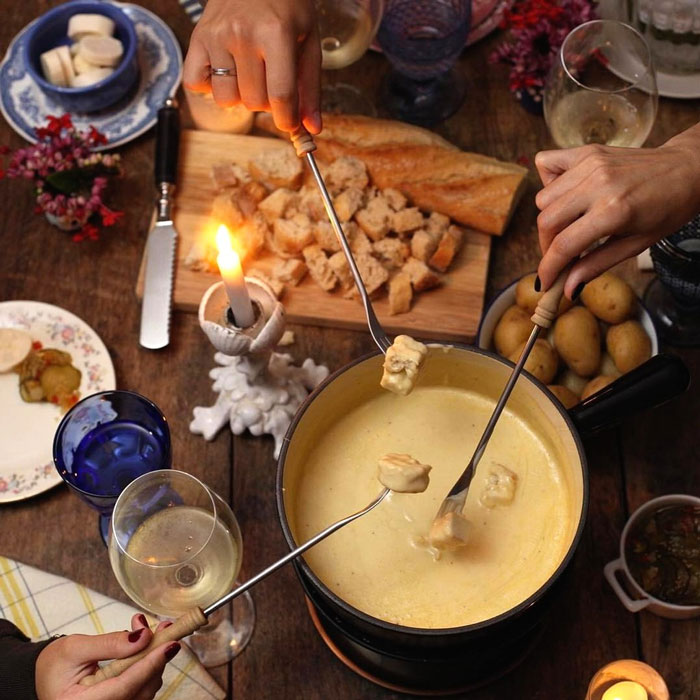 Hands dipping bread into cheese fondue at a cozy dinner, evoking nostalgia for old-school 'Watergate Salad' delicacies.