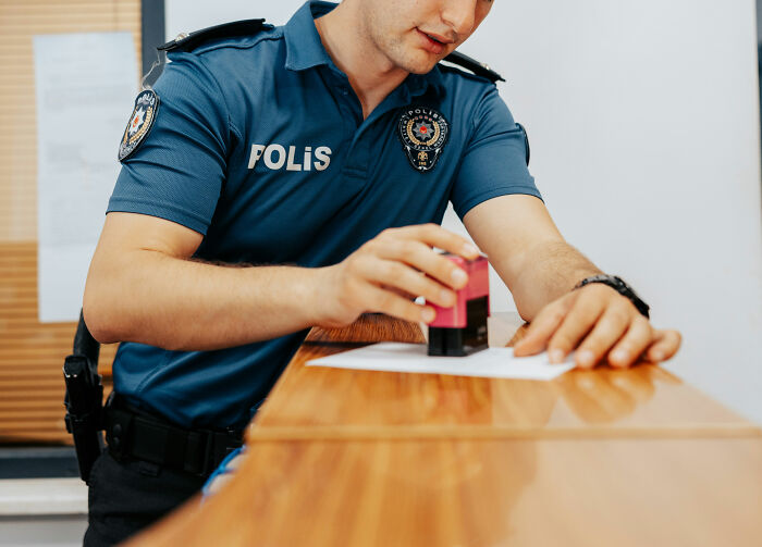 Police officer in uniform stamping documents on a wooden desk, challenging job misconceptions.