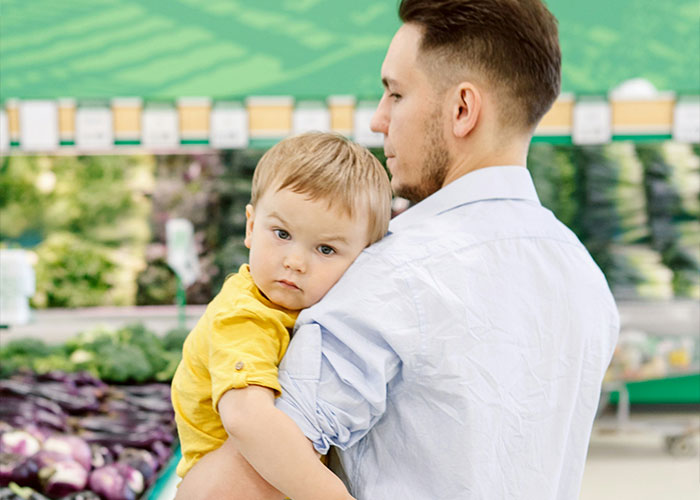 A man carries a child through a grocery store, highlighting parenting behaviors.