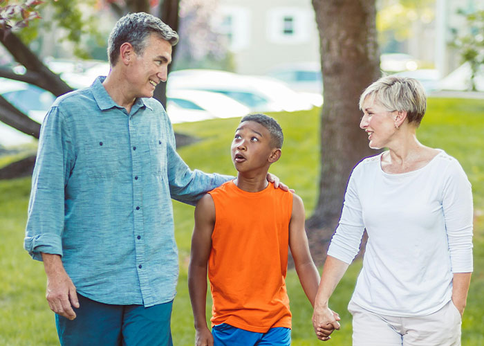 Family walking in park, smiling and holding hands, capturing reactions to coming out of the closet.