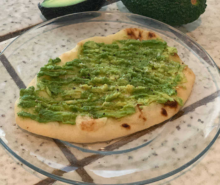 Lazy meal with mashed avocado on flatbread, served on a clear glass plate for a simple dining option.