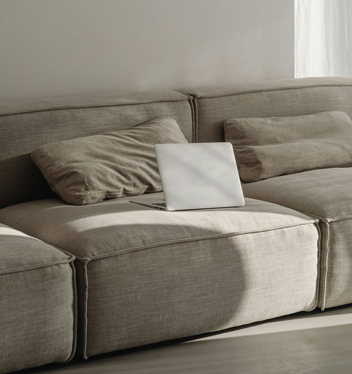 Laptop on a beige couch in natural light, showcasing home comfort.