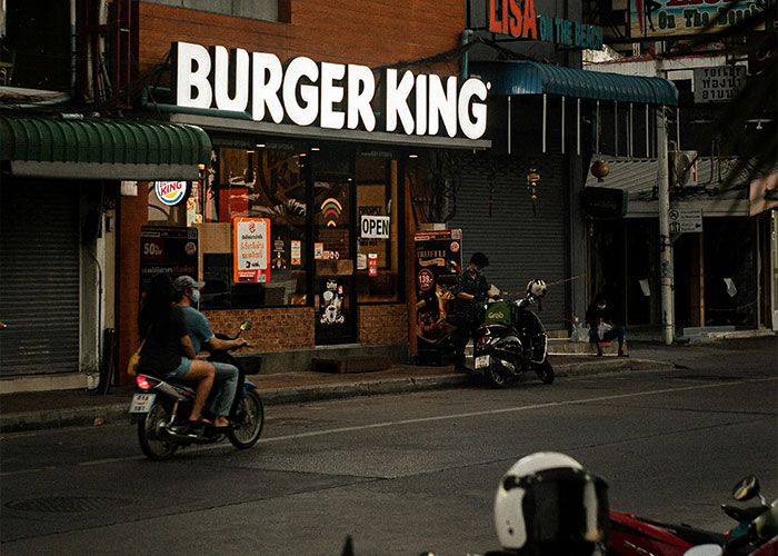 Burger King storefront at dusk with people on motorcycles passing by.