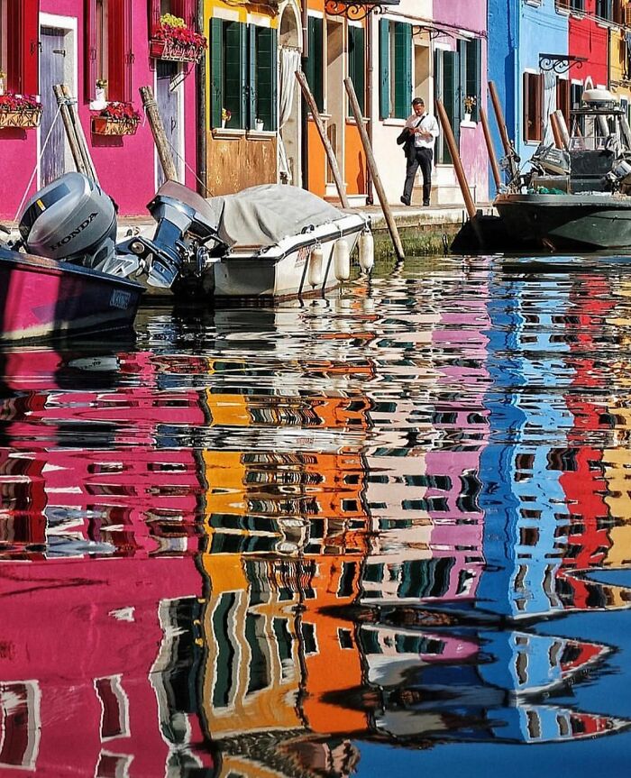 Colorful street reflection in water capturing an unexpected moment with a person walking by vibrant buildings.