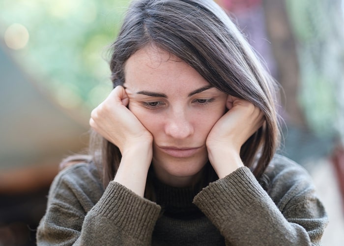 Woman looking thoughtful, pondering parenting mistakes, resting her face in her hands outside.