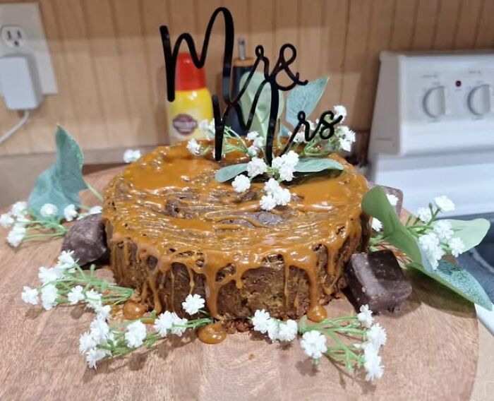 Wedding cake fail with caramel drizzle, decorated with flowers and a "Mr & Mrs" topper in a kitchen setting.
