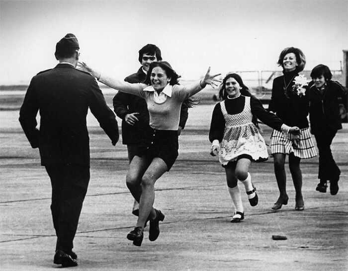 A black-and-white photo of people joyfully running towards a man in uniform with a dark history.