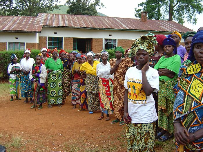 Women in colorful attire outside a rustic building, depicting historical community life.