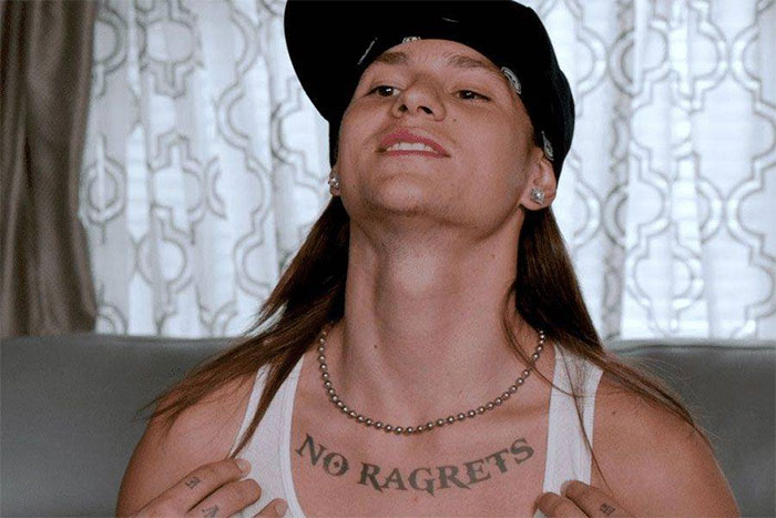 Person showing a "No Ragrets" tattoo on chest, symbolizing unattractive tattoos.