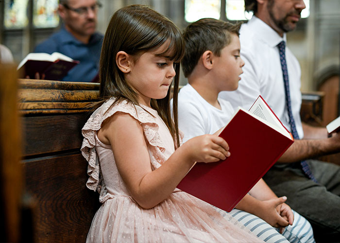 Child in a dress reading a book in a church pew, with a focus on parental behaviors and family.