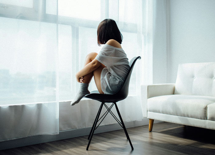 Woman sitting alone by a window, reflecting on mental health challenges.