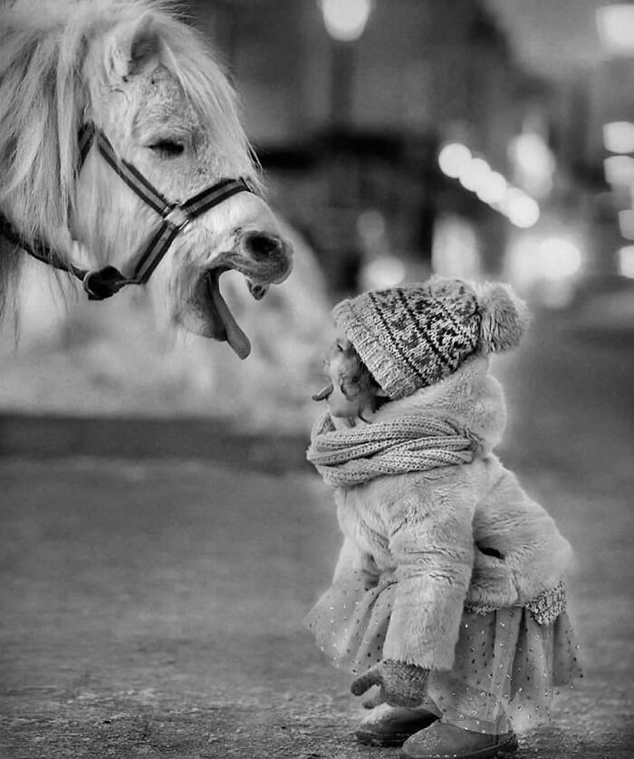 Child in winter clothes mimics a horse’s tongue gesture in a perfectly timed street photo capturing an unexpected moment.