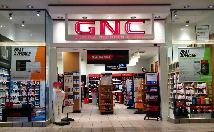 GNC store entrance, showcasing various health products and supplements, emphasizing employee firing practices.