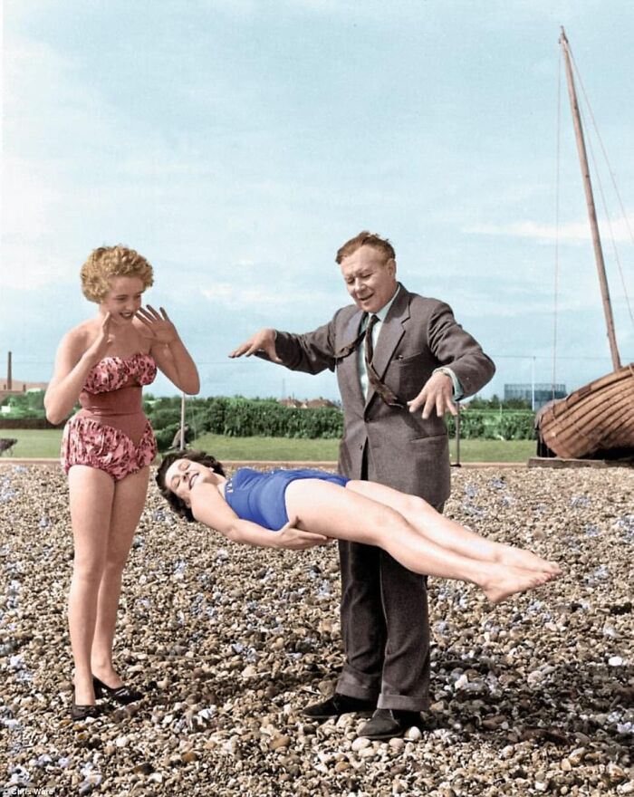Magician performing levitation on woman at the beach, capturing forgotten corners of history.