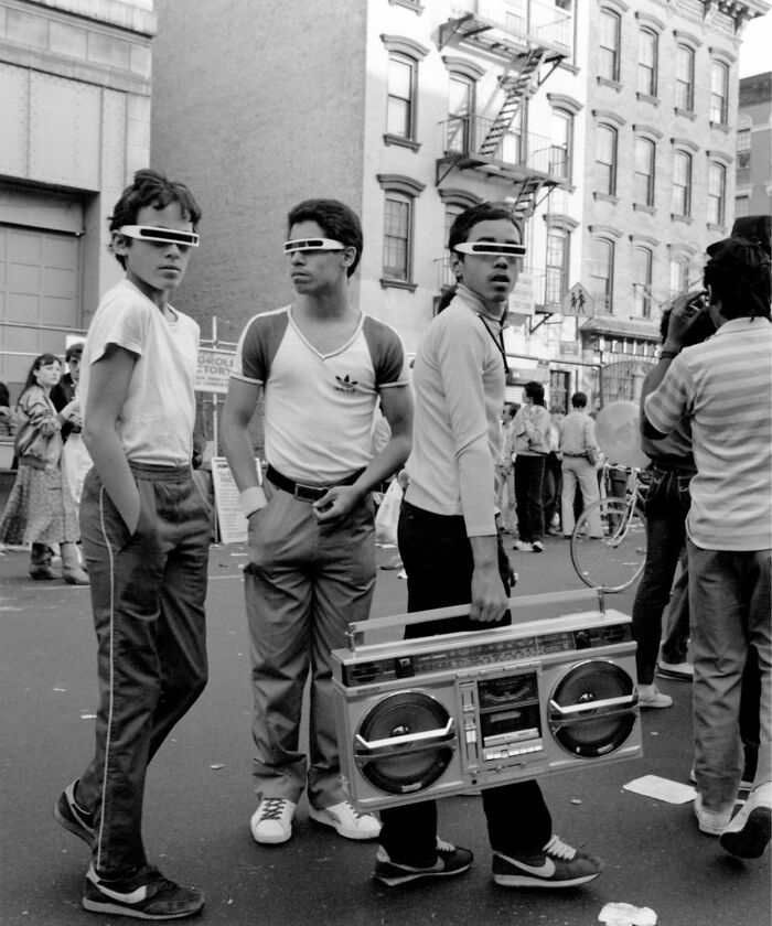 Three young men in retro sunglasses and casual outfits holding a boombox on a city street, capturing forgotten history.